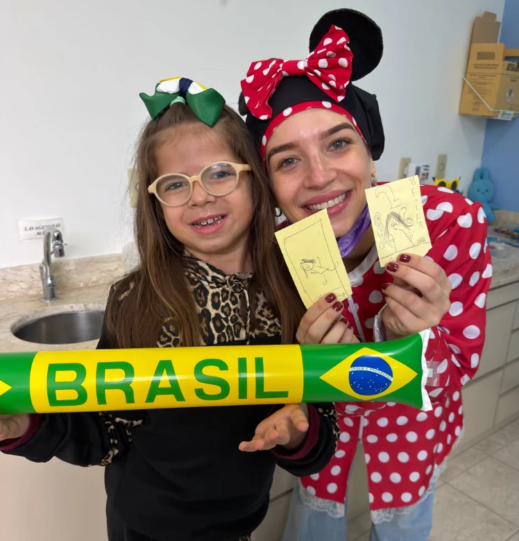 Dra. Rafaela Ayello com uma criança segurando desenhos feitos na consulta
